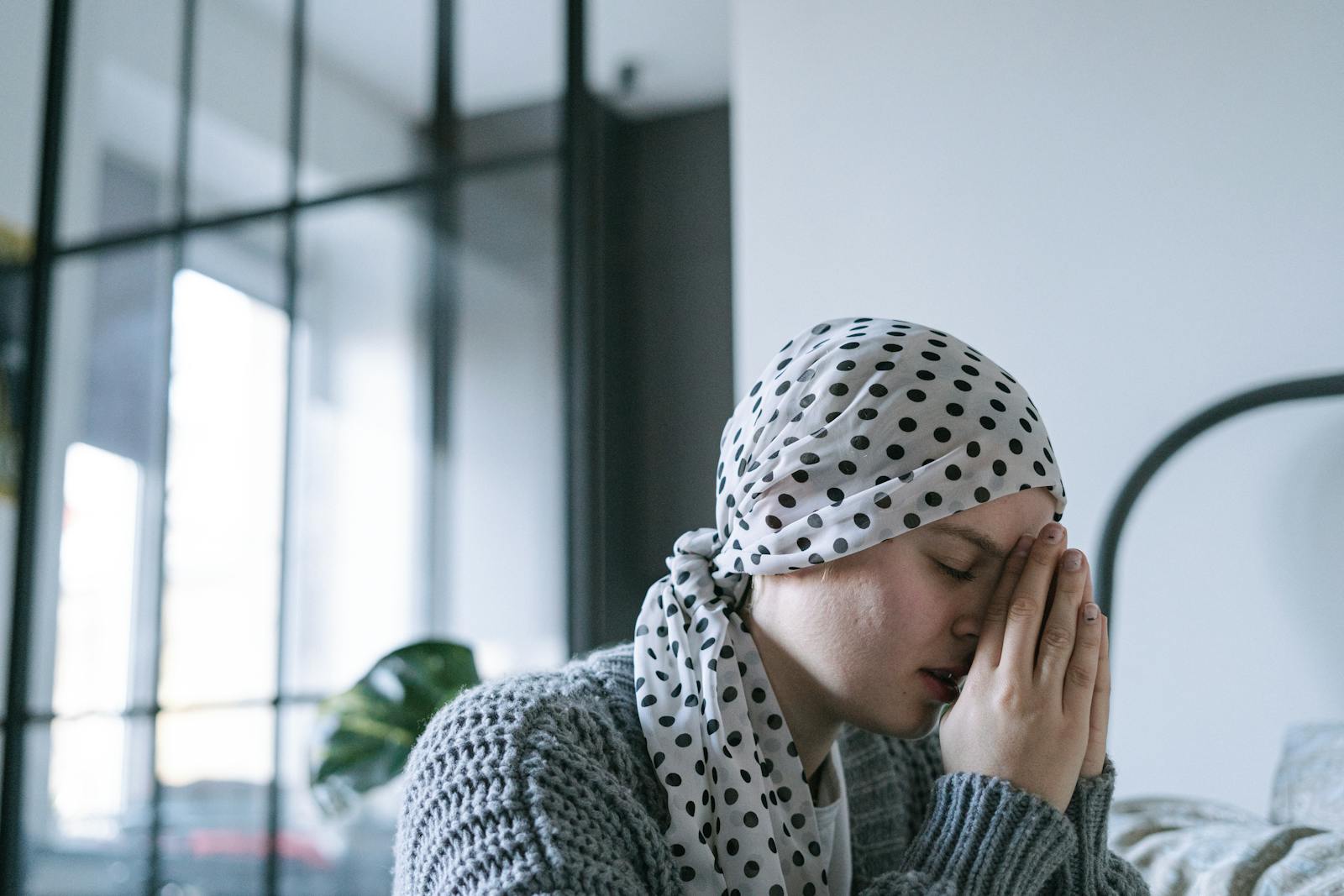 A woman wearing a polka dot scarf prays with hope, symbolizing strength and recovery during illness.