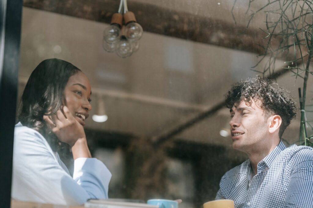 Two people enjoying a warm conversation through a cafe window, highlighting relaxed and friendly interactions.
