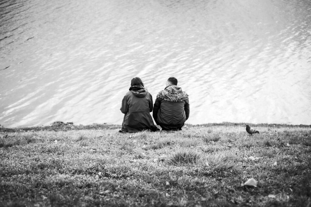 A couple in warm coats sitting by a serene lake, depicting a moment of tranquility.